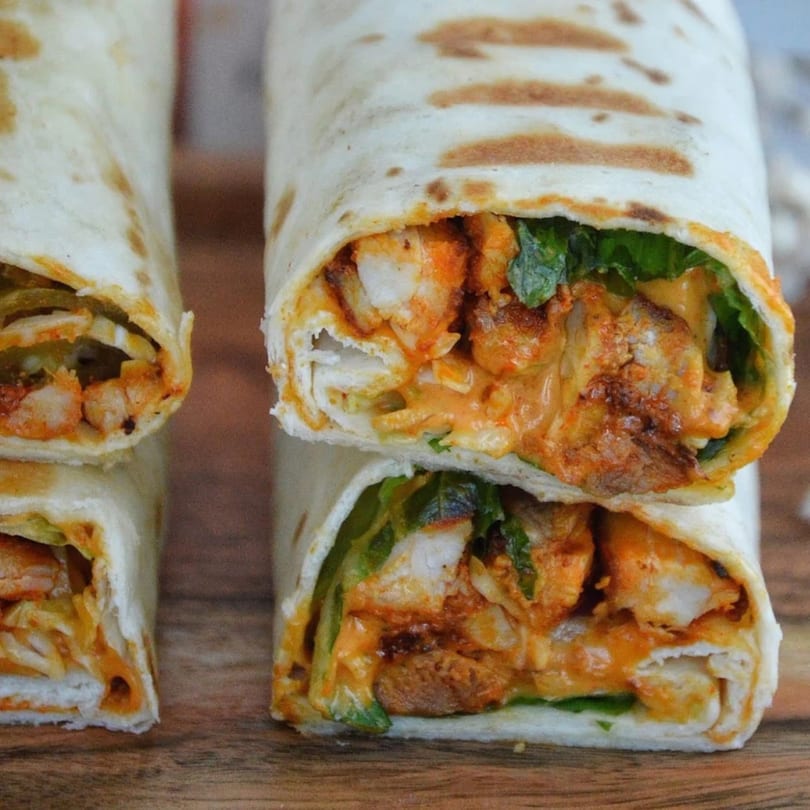 Two Cairos Gyros Tempe wraps, filled with chicken, sauce, and lettuce, on a wooden surface.