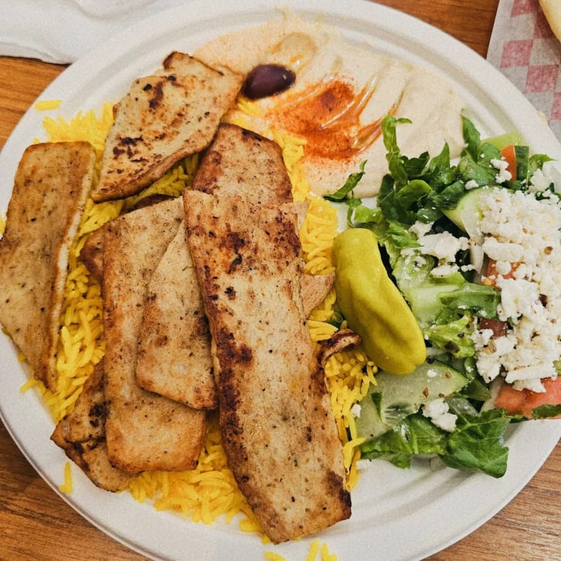 Cairos Gyros Tempe plate with sliced gyro meat, yellow rice, hummus, and a Greek salad.