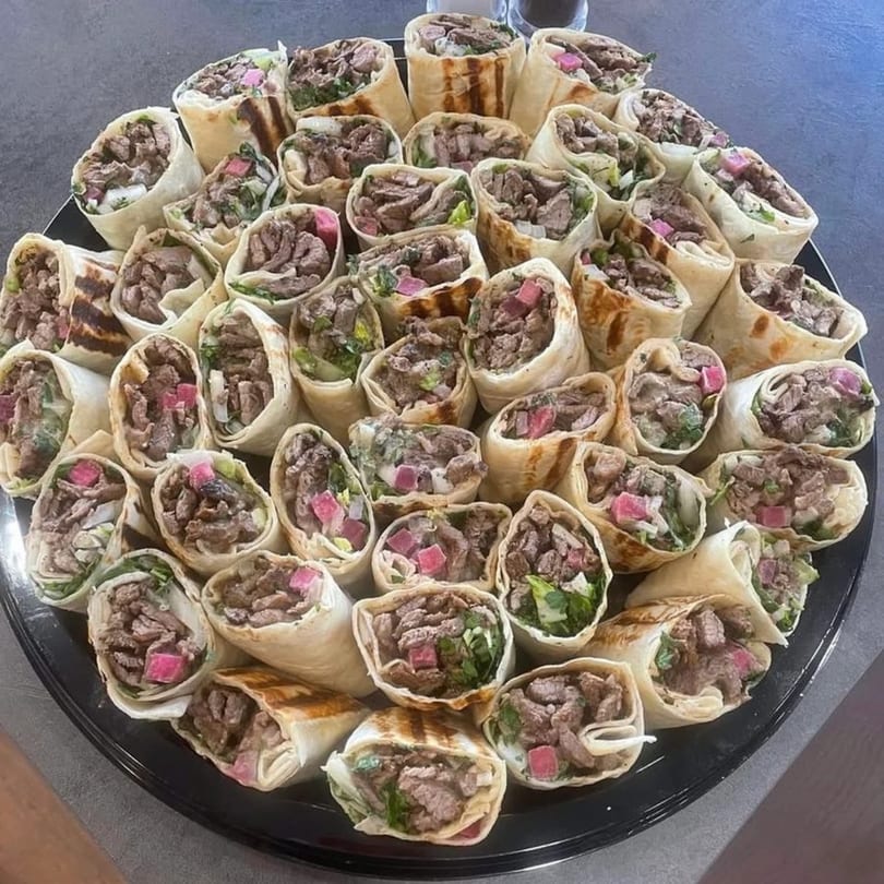 A large platter of Cairos Gyros Tempe's mini gyros, filled with meat, lettuce, and pink pickled vegetables.