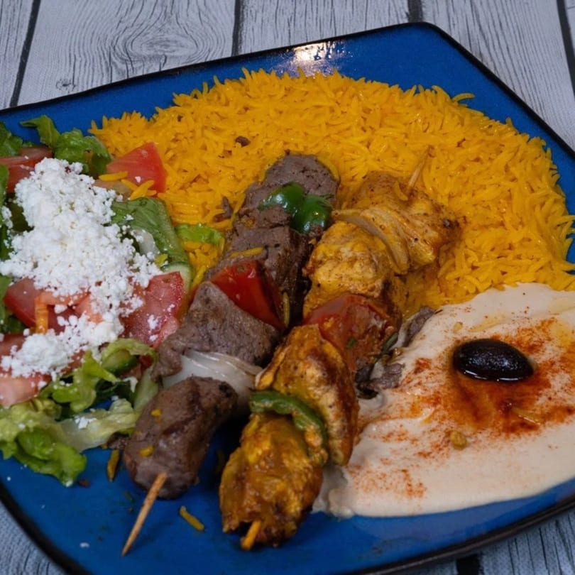 Cairos Gyros Tempe plate with two skewers of meat, yellow rice, salad, and hummus.