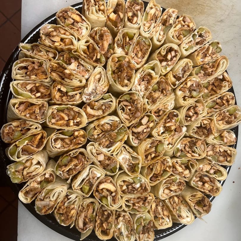 A catering platter filled with dozens of sliced Cairos Gyros chicken wraps, showcasing the fillings.
