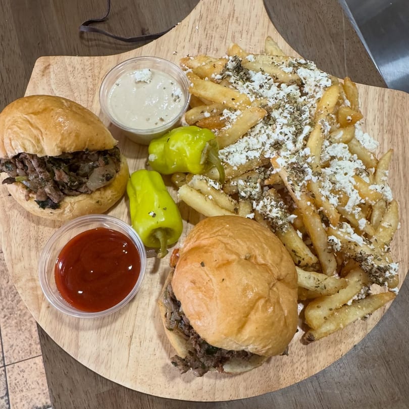 Two Cairos Gyros sliders, feta fries, two sauces, and two green peppers on a wooden board.
