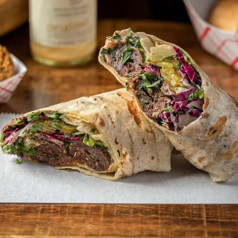 Two Cairos Gyros wraps, cut in half, revealing meat, red cabbage, and green herbs on a wooden table.